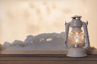 Gas lantern wooden board near heap snow through window