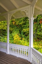 Wooden veranda with wooden floor and a white railing and beautiful autumn colours