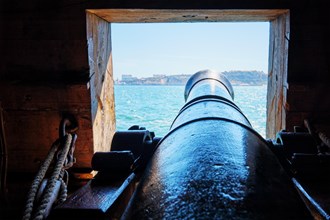 Sea view out of a gunport in hull of the ship over the gun cannon muzzle in on the gun deck of a sailing ship of Age of Sail