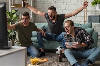 Front view cheerful male friends watching sports tv together while having snacks beer