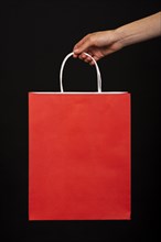 Close up hand holding red shopping bag black background