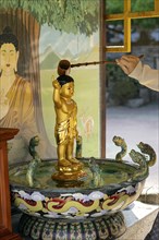 Person pours water over a small golden Buddha figure for prosperity and happiness