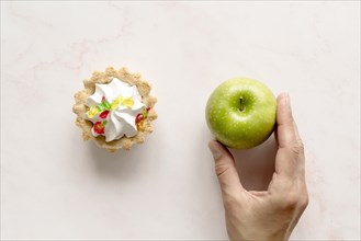 Human hand holding green apple near tart cake backdrop