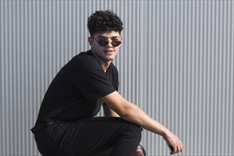 Young ethnic curly man sunglasses black clothes against grey wall