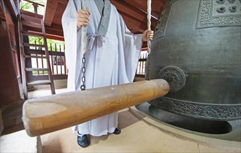 Korean monk strikes the bell with a wooden trunk
