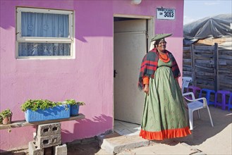 Herero woman in traditional colourful dress in front of her house in township near Swakopmund