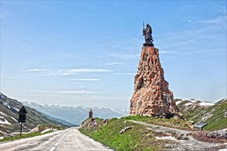 Photo with reduced dynamic saturation HDR of mountain pass alpine mountain road alpine road pass road pass above tree line with right monument with statue of Saint Bernard of Menthon on top of Little ...