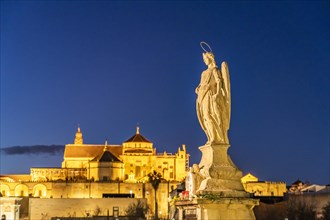 Statue of the Archangel Raphael on the Roman Bridge and the Mezquita at dusk