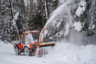Holder C9700H municipal tractor with snow blower clearing snow from road in forest after heavy snowfall in winter