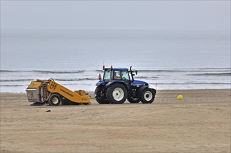 Tractor-pulled beach cleaner raking sea sand at seaside resort along the North Sea coast