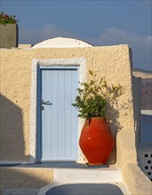 Red vase in front of yellow wall with blue door
