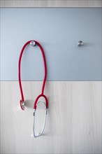 A red stethoscope hangs over a hook