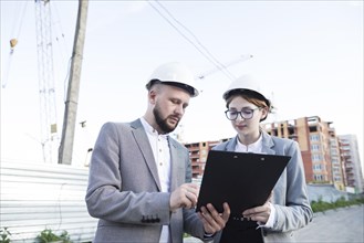 Young female male architect wearing hard hat looking clipboard