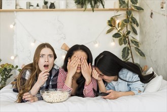 Girls lying bed eating popcorn having fun