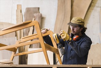 Male carpenter sanding wood with orbital sander workshop