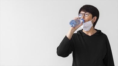 Woman with medical mask drinking water from bottle