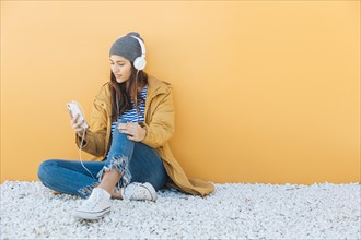 Woman sitting rug using smartphone listening music headphones