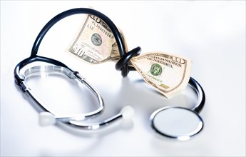 Stethoscope tied with dollar bills. High cost of medical health with stethoscope. Stethoscope wrapped around money isolated