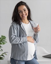 Smiley pregnant woman home holding glass water