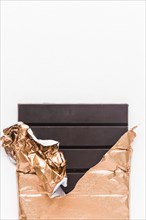 Delicious chocolate bar wrapped golden foil white background