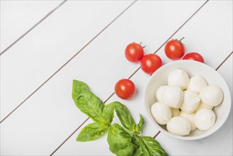 Mozzarella cheese ball with basil leaf red tomatoes wooden white background