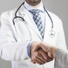 Close up male doctor shaking hand with patient against gray background