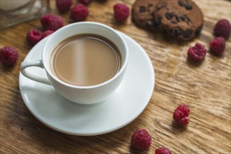 White cup coffee with chocolate cookies raspberries wooden background