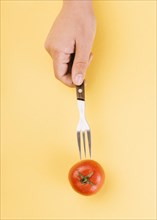 Human hand inserting fork red tomato yellow backdrop