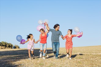 Family running field holding balloons