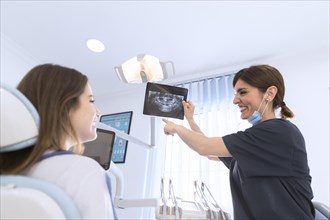 Happy smiling female dentist showing dental x ray patient