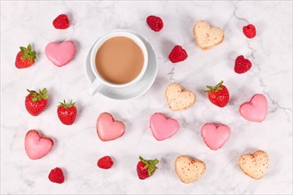 Pink and beige heart shaped French macaron sweets next to coffee cup and strawberry fruits