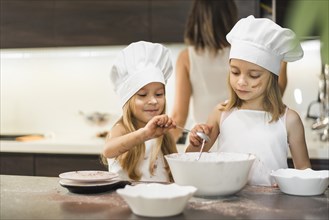 Little siblings chef hat mixing ingredients bowl kitchen worktop