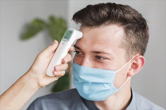 Man with medical mask checking temperature office with thermometer