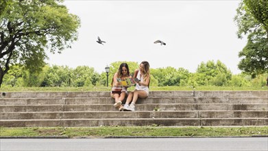 Two female tourist sitting staircase viewing map park
