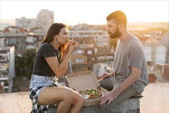 Side view couple eating pizza outdoors