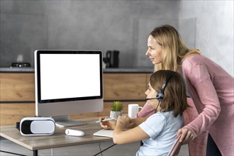 Girl with headset learning online with mother by her side