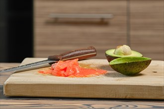 Thin slices of fresh avocado and smoked salmon on wooden cutting board