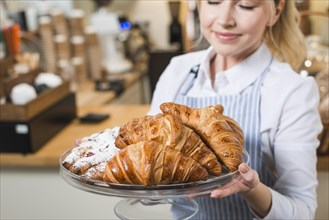 Close up smiling young woman smelling fresh baked croissants cake stand