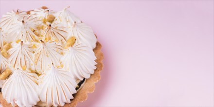 Close up lemon tart with italian meringue pink backdrop