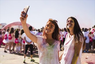 Portrait happy young women taking selfie mobile phone during holi festival