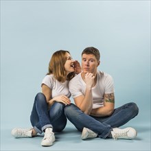 Portrait young woman telling secret his boyfriend against blue background