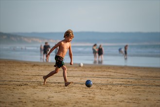Boy having fun playing running with ball on the beach of Atlantic Ocean. Fonta da Telha beach