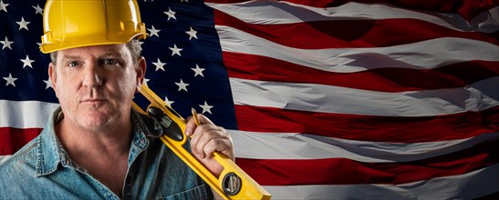 Male contractor wearing blank yellow hardhat over waving american flag background banner