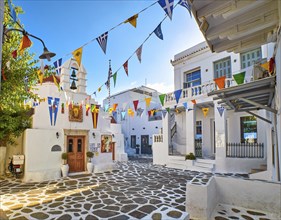 Beautiful morning view of small square decorated for some celebrations with flags in typical Greek town. Greek Orthodox church