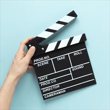 Person holding movie clapper blue background