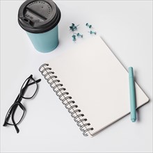 Disposable coffee cup pen eyeglasses spiral notepad thumbtack pins white background