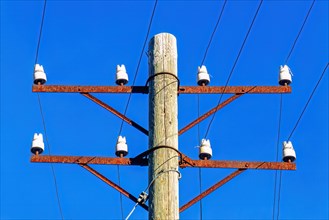 Old telephone pole with porcelain insulators and telephone wire at a blue sky