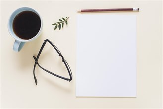 Coffee cup eyeglasses twig pencil blank white page beige backdrop
