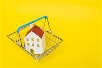 Overhead view house model inside shopping cart against yellow background