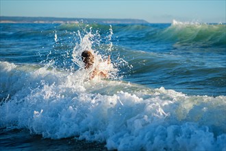 Boy has fun enjoys jumps dives in ocean sea waves of Atlantic Ocean. Fonta da Telha beach
